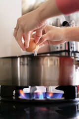 A person is cracking an egg into a pan on a stove. The pan is on a burner with a flame underneath it