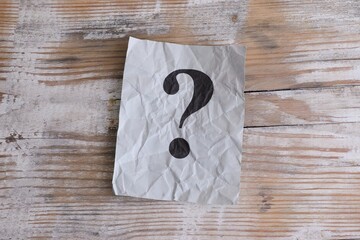 A gray crumpled paper note with a question mark on it on a wooden background. Close-up.