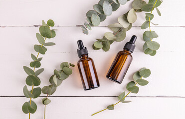 Two cosmetic bottles with a natural organic product based on eucalyptus oil on a white wooden background among eucalyptus branches. top view.