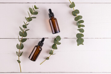 Two cosmetic bottles with a dropper with a cosmetic product for problem skin based on eucalyptus oil. white wooden background. top view.
