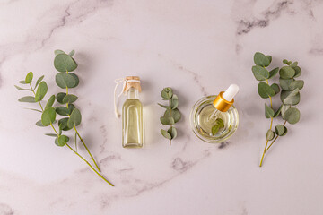 Bottle and bowl with pipette of natural organic eucalyptus oil on a white marble background with eucalyptus branches. Upper view. Spa treatment.