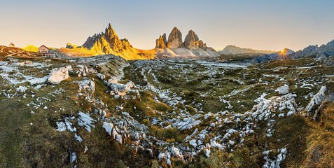 Panoramic shot of the peaks of Tre Cime di Lavaredo and Paternkofel illuminated by a golden sun at...