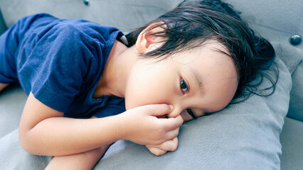 Asian child boy pinching nose with disgust on his face due to bad smell,something stinks,toddler gesture squeezing nose with fingers and laying on sofa, bad smell situation - Powered by Adobe
