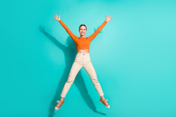 Full size photo of positive nice girl dressed orange shirt pants flying like star raising hands up...