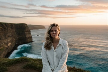 Woman Sitting on Coastal Cliffs at Sunset with Ocean Background