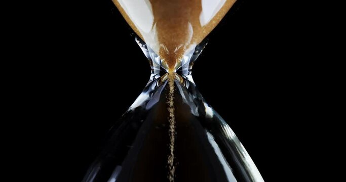 Hourglass. Sands move through hour glass. Sandglass close-up on a black background. Slow motion video. A pile of Golden sand at the bottom of the hourglass, small grains of sand fall from above.