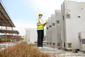 Engineer wearing safety helmet inspects precast concrete wall at construction site.