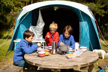 Happy family, kids, boy brothers and a dog, having breakfast in front of pitched tent in the...