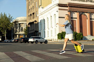 A girl, blonde, with a yellow suitcase on the street.