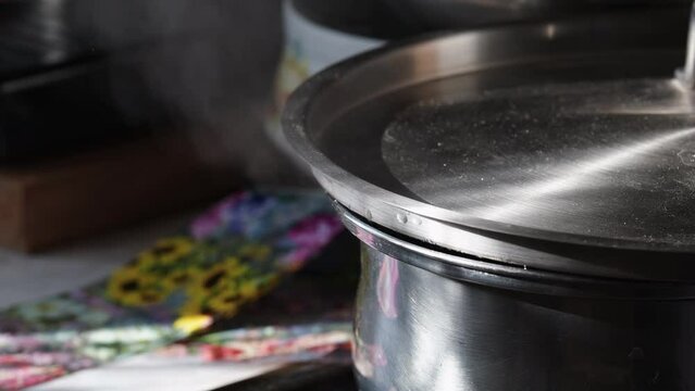 A saucepan of boiling water, covered with a lid, steam and water splashing out from under the lid. Home kitchen, a pan forgotten on the stove.