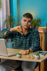 Dislike. Upset sad Indian business man at home office table showing thumbs down sign gesture, expressing discontent, disapproval dissatisfied bad work. Displeased Hispanic guy freelancer. Vertical