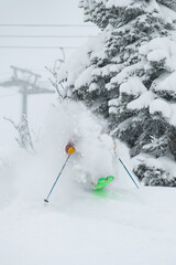 A skier in the forest in Siberia jumps out on bright skis from behind a tree in a cloud of raised snow with a chairlift in the background