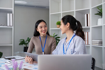 Two Asian women discussing a project in a modern office. Concept of teamwork, collaboration, and productivity