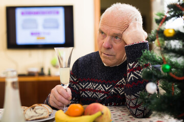 Lonely frustrated gray-haired senior man sitting at home table during Christmas celebration