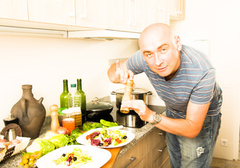 Male prepares two salads and fills them with pepper on home kitchen