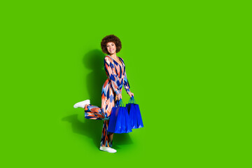 Photo of charming glad nice woman wear trendy print clothes hands hold bags isolated on vibrant green color background