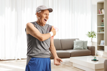 Elderly man in sportswear at home suffering from pain in the shoulder