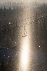 Chair lift at a ski resort in a column of bright sunlight and sparkling snowflakes with trees in the background