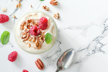 Greek Yogurt with Fresh Raspberries and Nuts. A delightful serving of Greek yogurt topped with fresh raspberries, pecans, and walnuts, garnished with mint on a marble background.