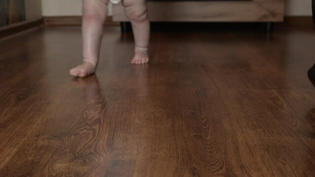 The baby's bare feet stomp on the parquet floor. Close-up. Slow motion. An unrecognizable baby walks barefoot on a wooden parquet floor. High quality 4k footage