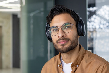 Portrait of a young man with glasses and headphones in modern office setting