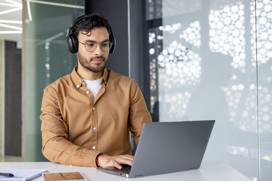 Focused man working on laptop wearing headphones in modern office