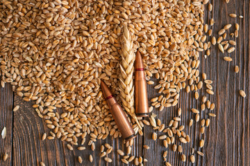 Wheat grains are spread across a wooden table, interspersed with several metal bullet shells. The...