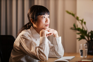 A japanese businesswoman sitting at home office and looking at computer monitor late at night.