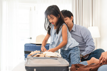 Happy Asian family preparing for journey. Father looking at cute daughter packing suitcases with...