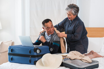 Happy Asian senior couple preparing for journey. Elderly man and woman fitting clothes, planing,...