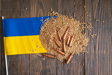 Wheat grains with yellow and blue Ukrainian flag on wooden background with several metal bullet shells. The concept of the photo suggests that grain can be used as a weapon. Hunger as a weapon