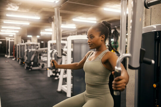 A fit black sportswoman is practicing chest on exercise machine in a gym.