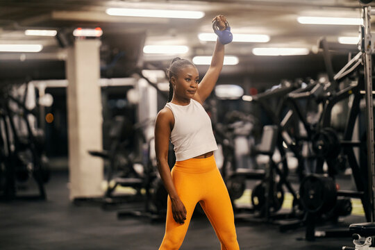 A black sportswoman in shape is practicing her shoulder with kettle bell at the gym.