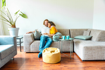 Cheerful multiracial couple sitting on sofa in the living room - Happy family moving in new home -...
