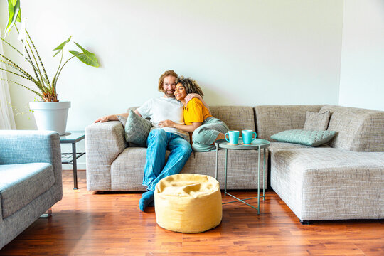 Cheerful multiracial couple sitting on sofa in the living room - Happy family moving in new home - Real estate and stylish furniture concept