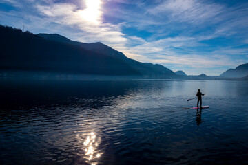 Man on a Paddleboard on Lake Lugano with Sunlight and Mountain in Ticino, Switzerland.