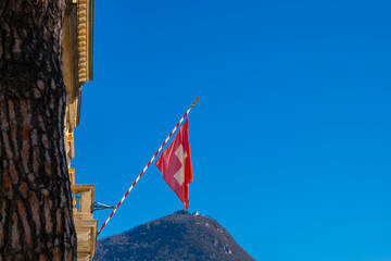 Swiss Flag and Mountain Peak Monte Bre Against Blue Clear Sky in a Sunny Day in Lugano, Ticino,...