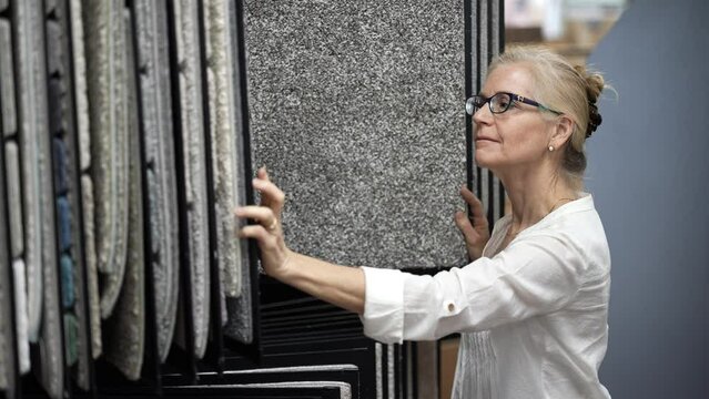 Attractive mature woman shopping for carpet looking through samples for home redecorating project, in a hardware store.