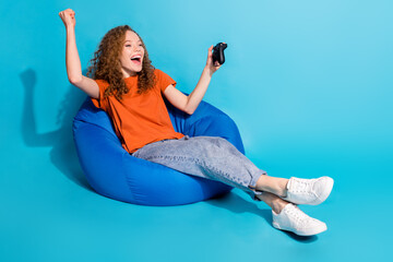 Photo of crazy positive girl sit bean bag win play game isolated blue color background