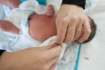 Newborn baby being dressed by an adult in a soft white outfit, focusing on the careful and loving process of dressing a newborn, with the baby's tiny hands and feet visible, symbolizing new life