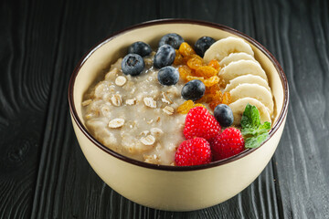 tasty nutritious oatmeal with fruits and berries on a black wooden rustic background