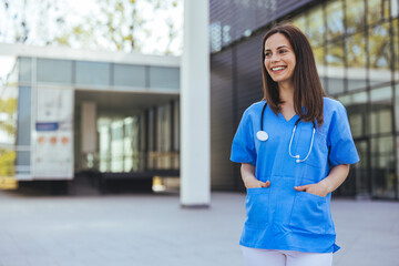 A joyful Caucasian nurse in blue scrubs stands confidently outside a hospital, stethoscope around...