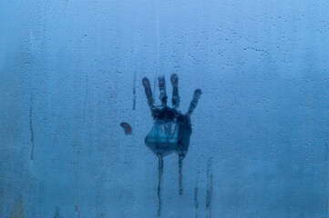 Palm print on foggy glass with water drops. Background is deep blue and gives gloomy impression