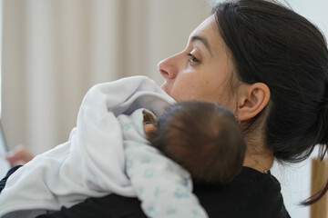 Young mother holding her newborn baby close to her shoulder, both appearing calm and connected,...