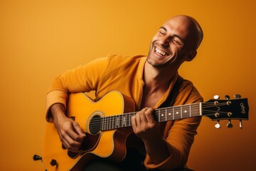 Portrait of a grinning man in his 30s playing the guitar in front of soft orange background