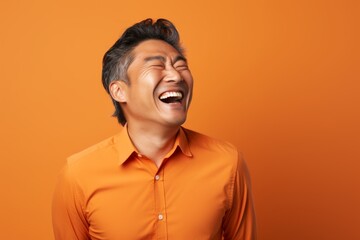 Obraz premium Portrait of a glad asian man in his 40s laughing in soft orange background