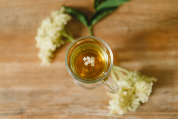 A clear glass mug filled with elderflower tea is placed on a rustic wooden table. Fresh...