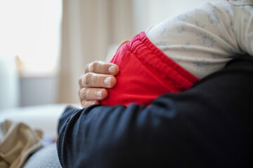 Close-up of a mother’s hand gently cradling her newborn baby dressed in red pants. The image...