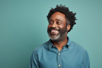 Fototapeta premium Portrait of a grinning afro-american man in his 40s smiling at the camera over soft teal background
