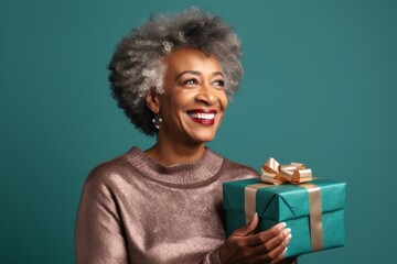 Portrait of a glad afro-american woman in her 50s holding a gift over soft teal background